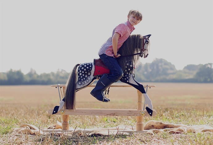 Young boy riding english dapple grey rocking horse outside in a field