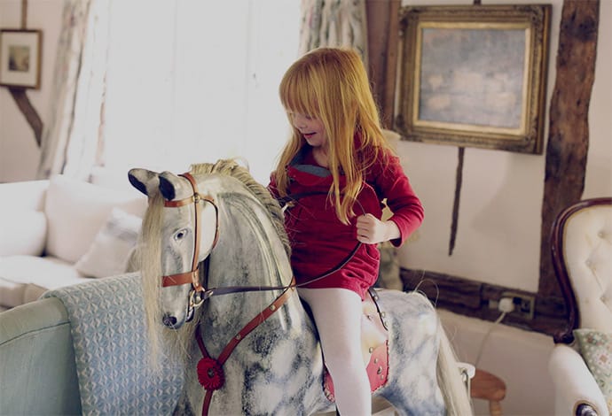 Young girl riding an english dapple grey rocking horse inside